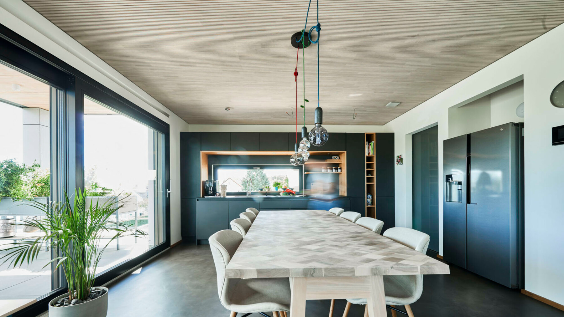 Der großzügige Esstisch dieser Wohnung in dem Nürtinger Klimaholzhaus fasst die Farbe der hellen LIGNO® Decke in Weißtanne auf  und bildet einen klaren Kontrast zu dem dunklen Boden. 
