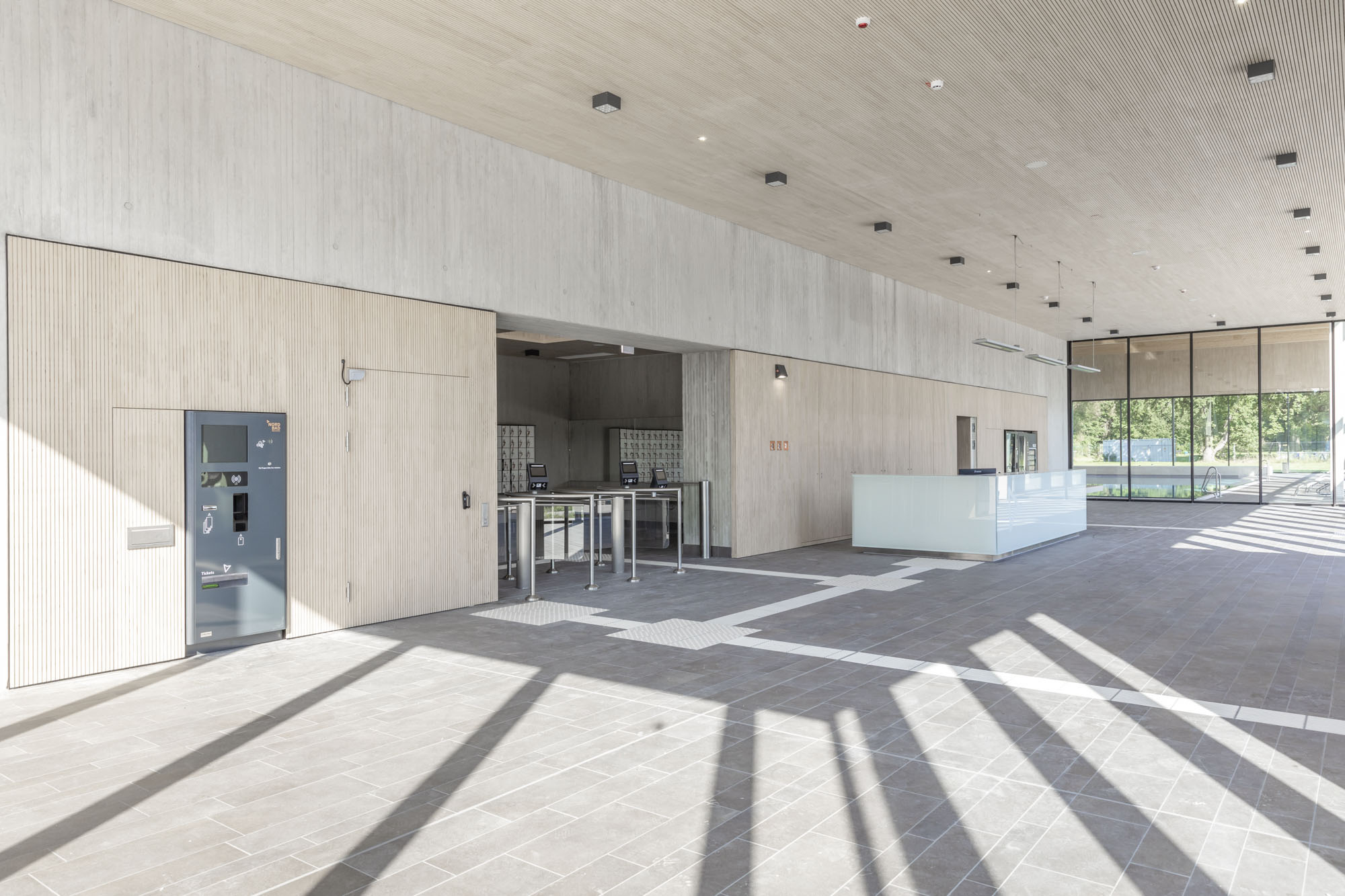 Direkt an das helle Eingangsfoyer schließt ein massiver Gebäudekern aus Stahlbeton an, in dem unter anderem die Umkleiden und Sanitärbereiche untergebracht sind. Er unterstützt die Aussteifung der Holzarchitektur für die Dachlandschaft. Paneele LIGNO® Akustik light zieren hier die Decken und Wände aus Beton, erfüllen akustische Aufgaben und integrieren Schrank- und Türöffnungen. 