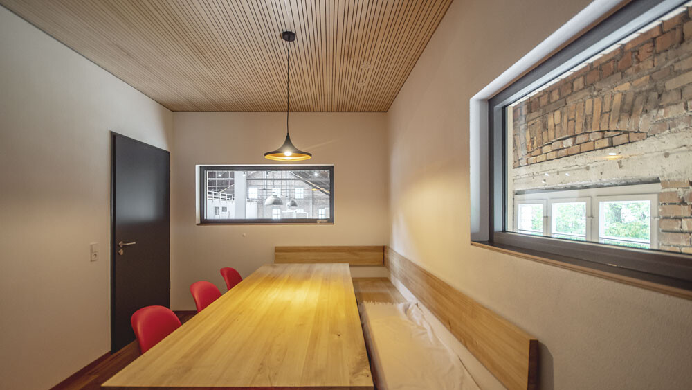 Dieses Zimmer mit Tisch und roten Stühlen wird dominiert durch die verschiedenen Holztöne von Boden, Tisch und Decke, welche durch das warme Licht der Hängelampe verbunden werden. 