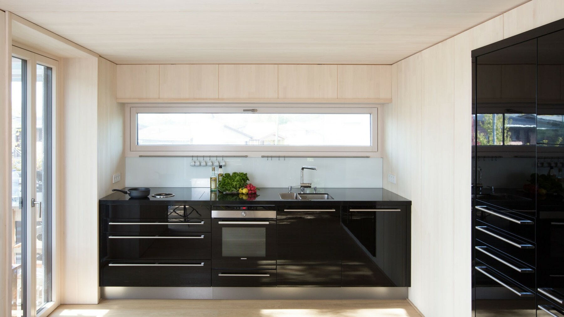 Das Schwarz der Küchenzeile bildet einen aufregenden Kontrast zu dem Hellen Ton der Holzverkleidung aus Weißtanne. 