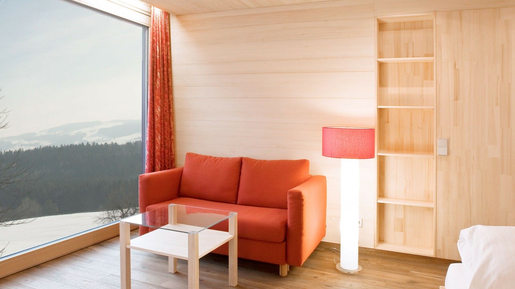 Das in Holz gekleidete Hotelzimmer gewährt durch ein, die Wandseite einnehmendes Panoramafenster, wunderschöne Ausblicke in die Natur. 