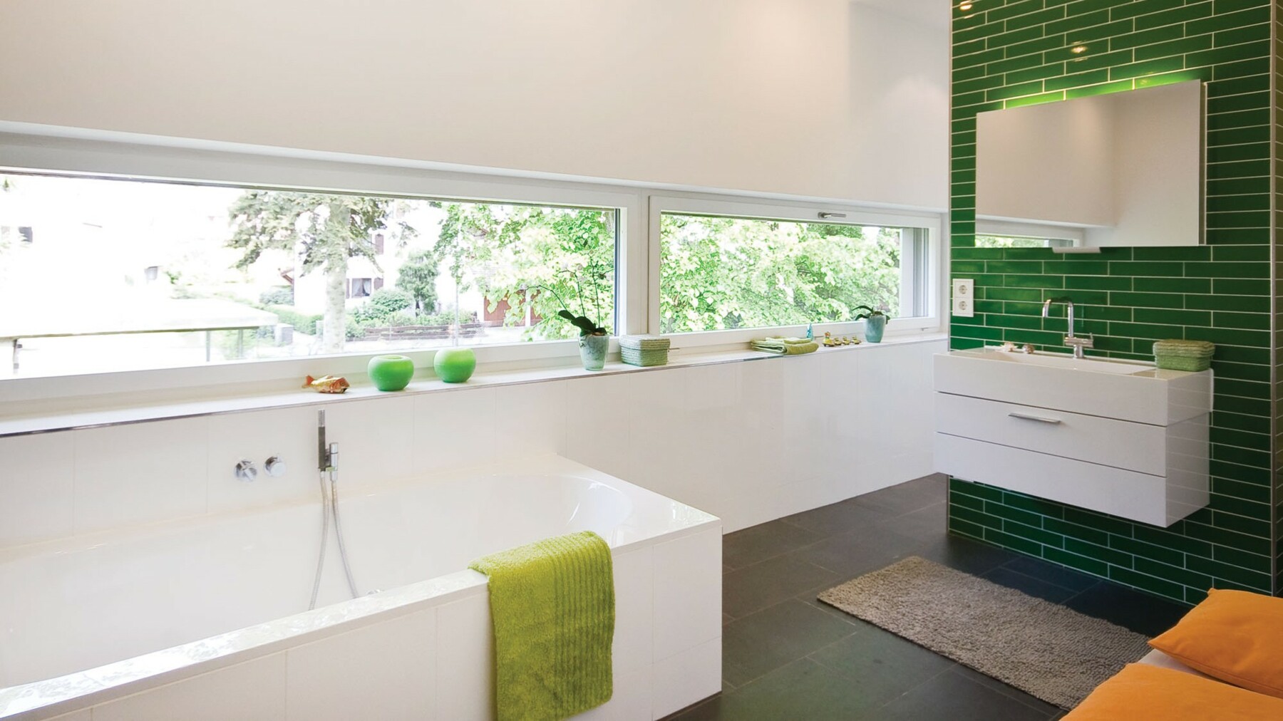 Im Badezimmer sorgt eine grün gekachelte Wand für einen besonderen Farbakzent und durch ein lang gezogenes Fensterband fällt viel Licht in den Raum.