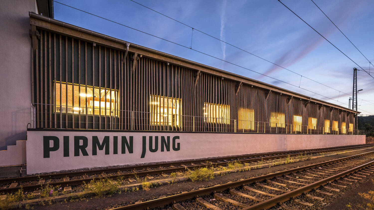 Die umgebaute, alte Bahnhofshalle wird eingerahmt durch vertikal angeordnete breit gefächerte Holzleisten und spiegelt die Struktur der im Inneren eingesetzten Akustik Light wieder.