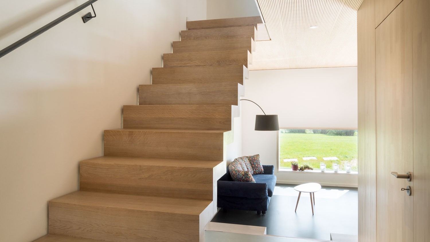 Die offene Holztreppe ins Obergeschoss schließt an die Decke aus fein profilierten Akustikpaneelen an und verleiht dem Raum durch die offene Bauweise einen dynamischen Charakter. 