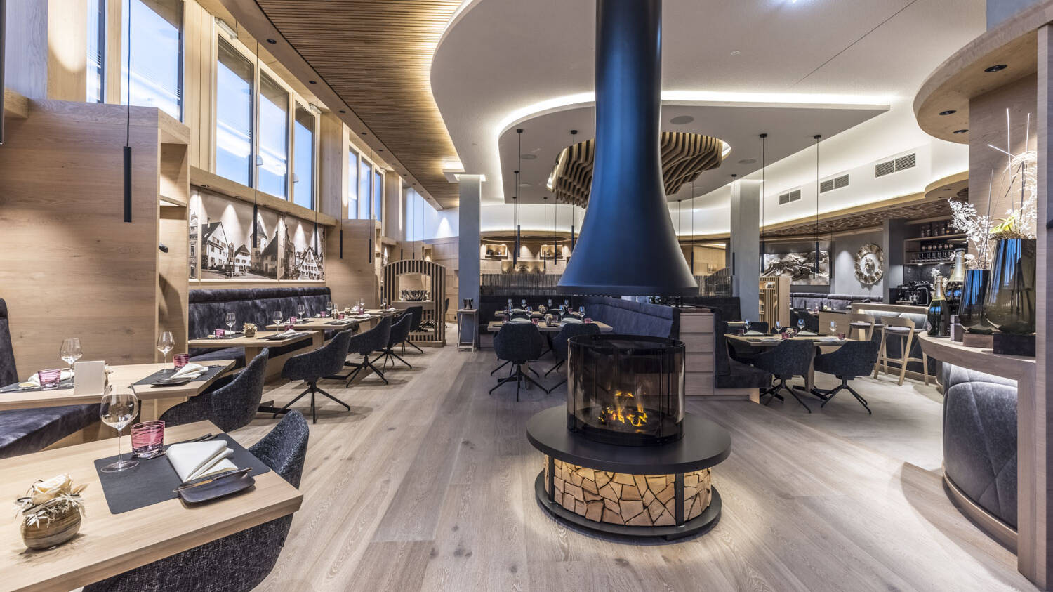 Runde Formen, viel Einsatz von Holzmaterialien und ein offener Holzofen in der Mitte des Raumes verleihen dem Restaurant eine zugleich heimelige und elegante Atmosphäre.