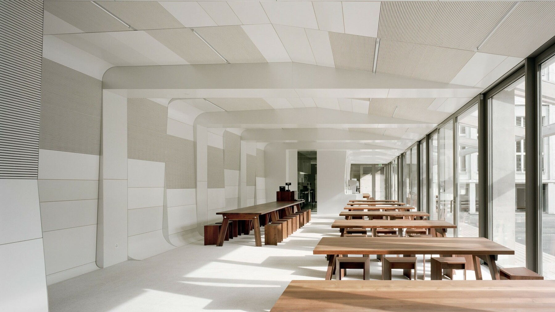 Das Sichtbeton-Tragwerk der Mensa verkleideten die Architekten komplett mit weiß und grau lackierten Holzpaneelen made of LIGNO®, welche einen reizvollen Kontrast zum dunklen Holzton der Tische und Stühle bilden.