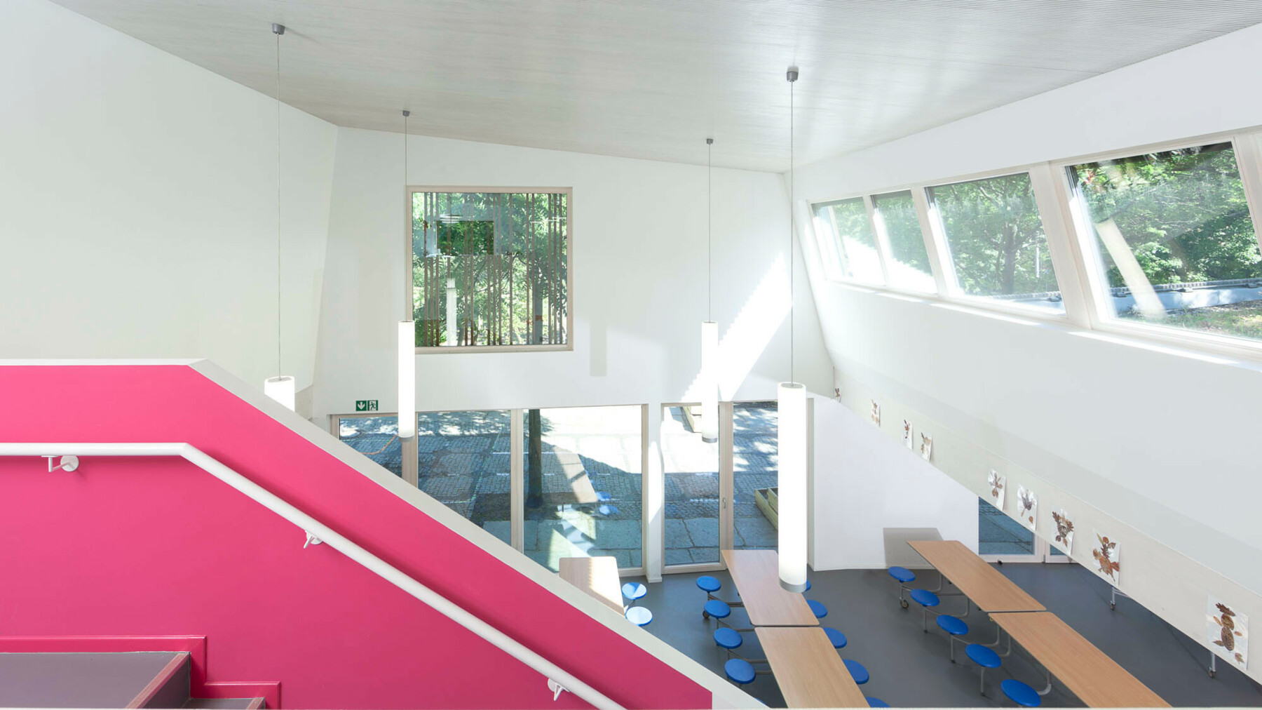 Eine breite Treppe führt von der Mitte des Speisesaals hoch in die Galerie und dient durch die pinke Anstreichung als kontrastreicher Blickfang in dem ansonsten weiß gehaltenen Raum.