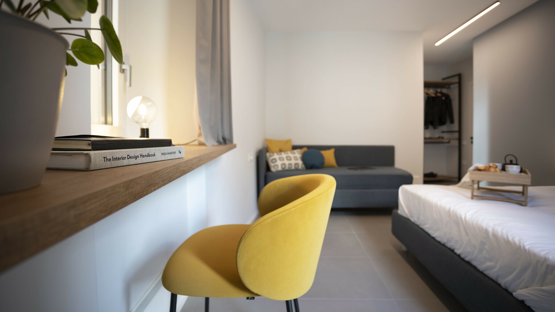 Der moderne Stuhl in Senfgeld bildet einen farblichen Akzent in dem ansonsten in gedeckten Naturtönen gehaltenen Hotelzimmer. 