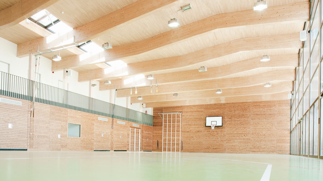 Die in Holzrahmenbauweise errichtete Sporthalle ist zum Teil mit hochwirksamen Massivholzoberflächen aus LIGNO® Akustikpaneelen ausgestattet, die den schallharten Oberflächen Glas und Beton entgegenwirken. 