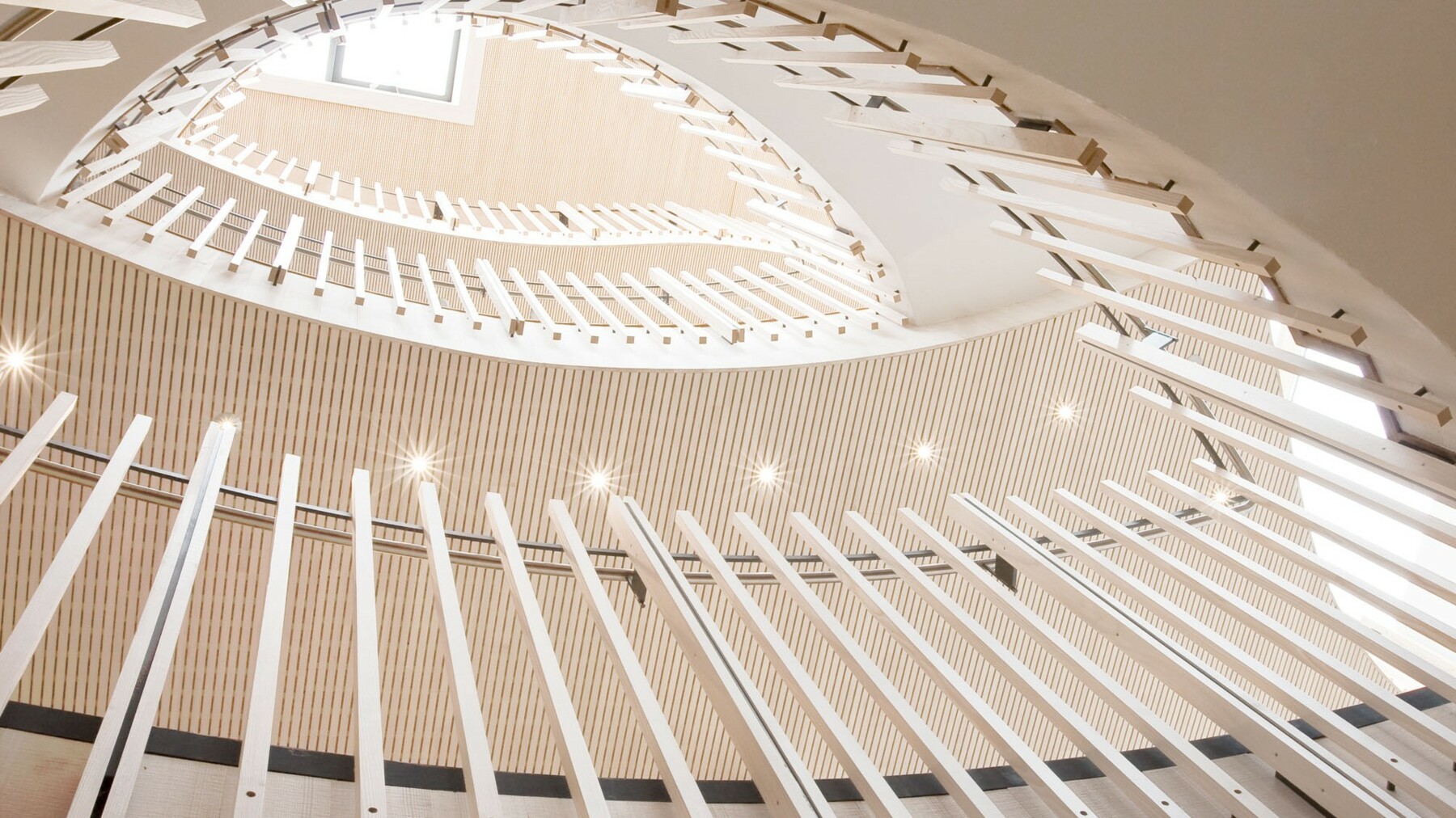 Die skulpturartig geschwungene Treppe wird gesäumt von senkrechten Tannenstäben und fasst somit die feine Profilierung der Holzverkleidungen im Rezeptionsbereich auf. 