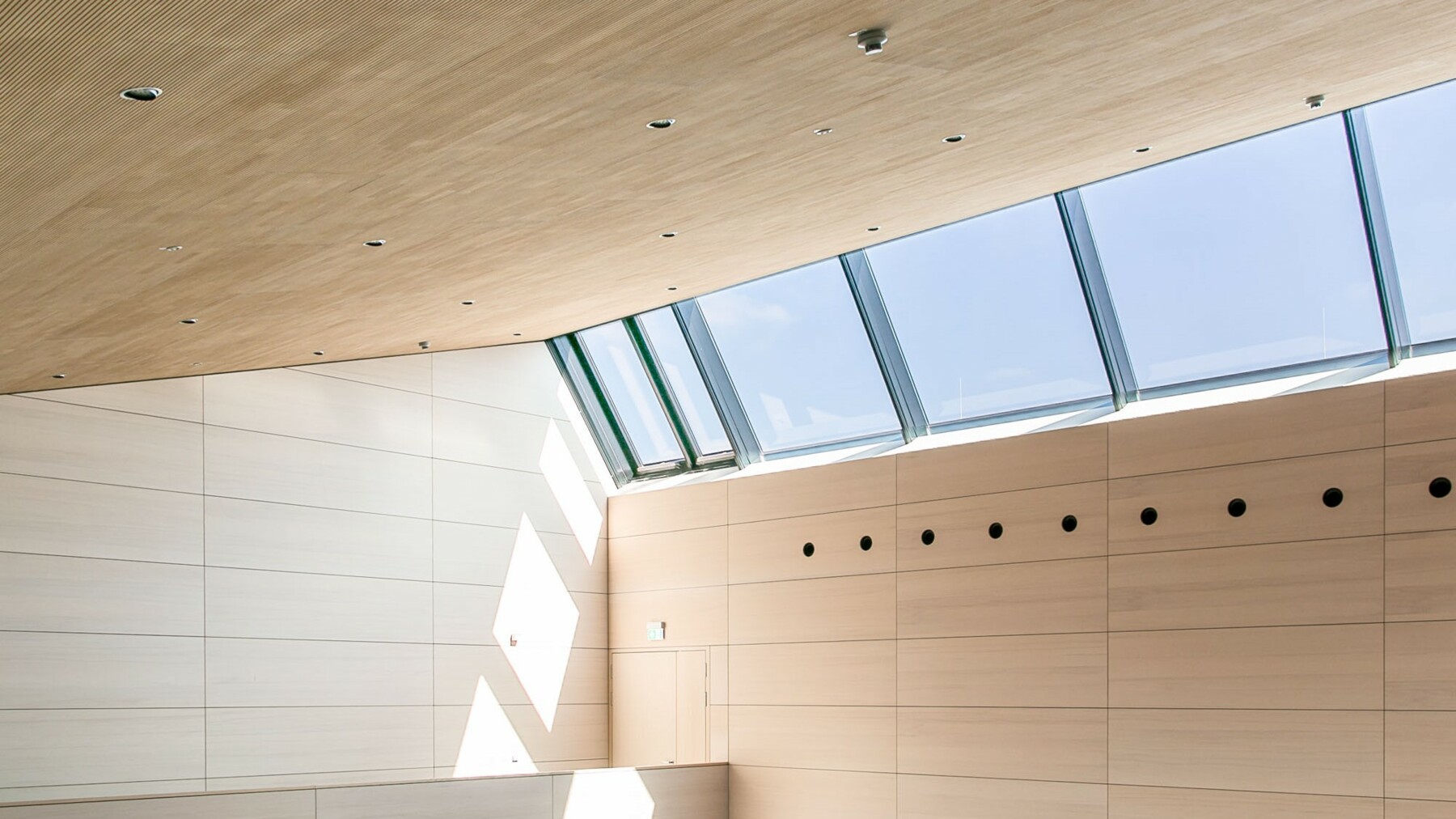 Schräge Dachfenster lassen viel Licht in die abgestufte Mehrzweckhalle und sorgen zusammen mit der hellen Holzverkleidung von Lignotrend für eine angenehme Raumatmosphäre. 