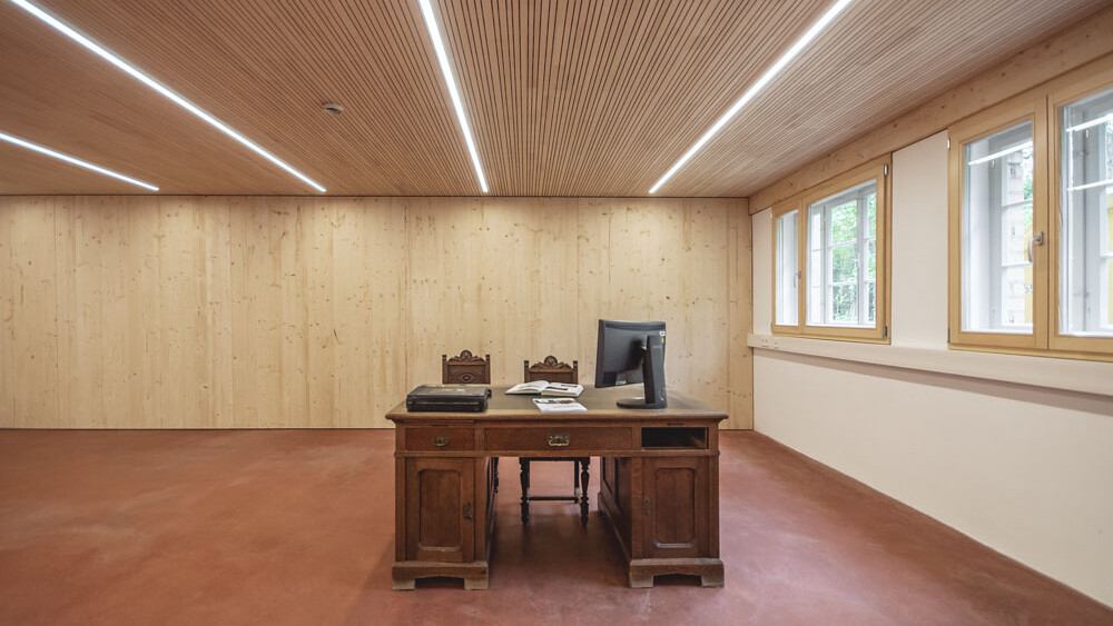 Dieser minimalistisch eingerichtete Raum besticht mit kupferrotem Boden im Zusammenspiel mit der lebhaft profilierten Decke aus edler Weißtanne. 