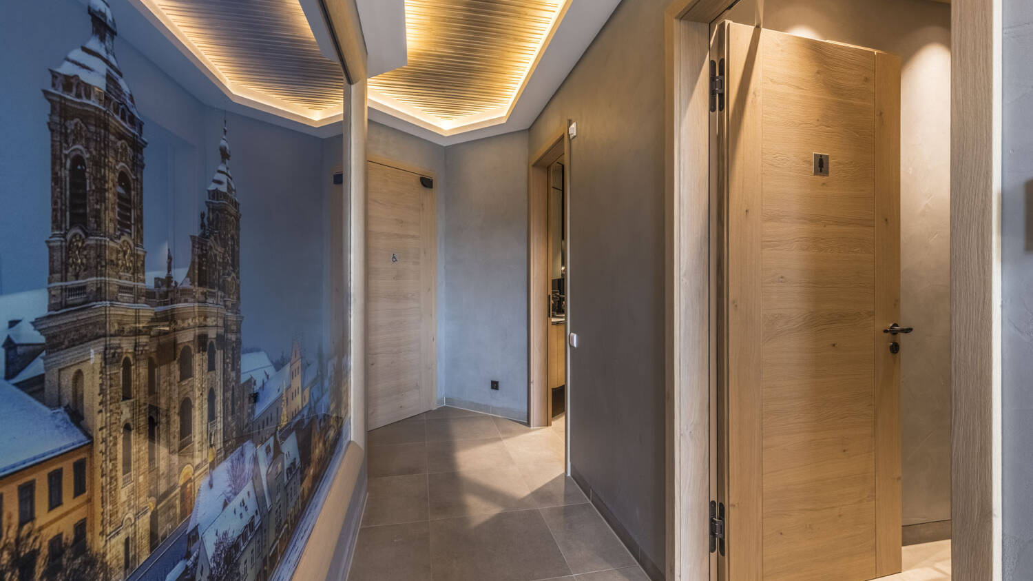 Auch im Gang zum WC-Bereich führt ein Zusammenspiel aus Holz, Stein und elegantem Licht zu einem dynamischen Raumgefühl.  